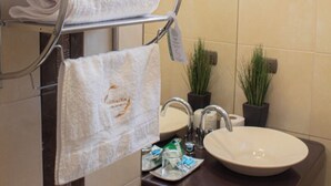 A bathroom with a metal towel rack holding folded towels, a sink with a large mirror, and two potted plants on the counter. - Alsacia Boutique Hotel (Arequipa)