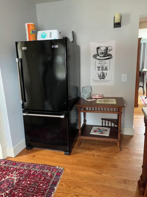 Compact kitchen area with a refrigerator, table, and chair, featuring a framed poster and a book.