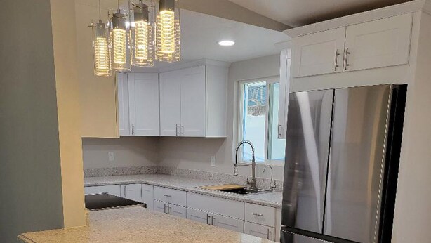 A modern kitchen with white cabinets, a granite island with bar stools, stainless steel appliances, and pendant lighting. - Beautiful peaceful quiet country living 

 (Holtville)
