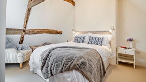 Ein Schlafzimmer mit einem großen Bett, einem Nachttisch, einem Sessel und freiliegenden Holzbalken.