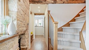 Eine Treppe mit Holzgeländer und Teppichstufen führt zu einem Raum mit Steinwand und Holzbalkendecke.