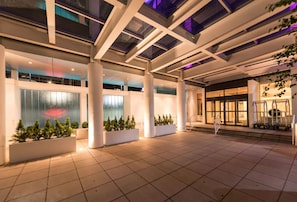 A spacious indoor area with a modern architectural design, featuring large pillars, a tiled floor, and a glass facade with a reflection of lights. - Hotel Noma Trademark Collection By Wyndham (New Rochelle)