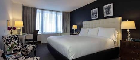 Una habitación de hotel con una cama grande, un escritorio, una silla, un aparador y dos lámparas.