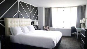 A hotel room with a large bed, a desk, a chair, a lamp, and a window with curtains. - Hotel Noma Trademark Collection By Wyndham (New Rochelle)