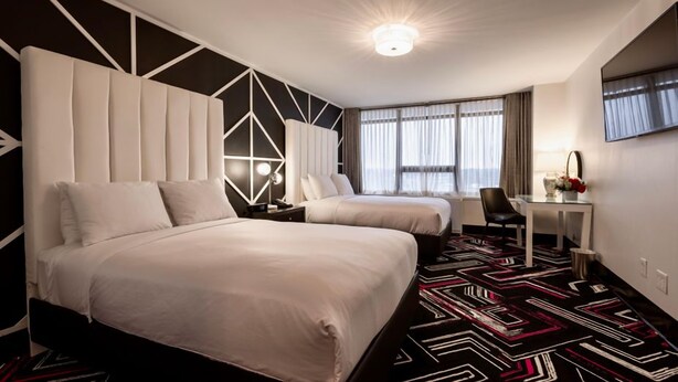 A hotel room with two beds, a desk, a chair, and a large window with curtains. - Hotel Noma Trademark Collection By Wyndham (New Rochelle)