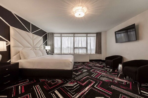 A modern hotel room with a large bed, a TV mounted on the wall, and a patterned carpet. - Hotel Noma Trademark Collection By Wyndham (New Rochelle)