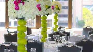Uma área de refeições com mesas dispostas para um evento formal, destacando vasos altos com flores e maçãs verdes.