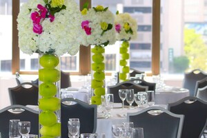 Un comedor con mesas dispuestas para un evento formal, con altas flores en jarrones y manzanas verdes.