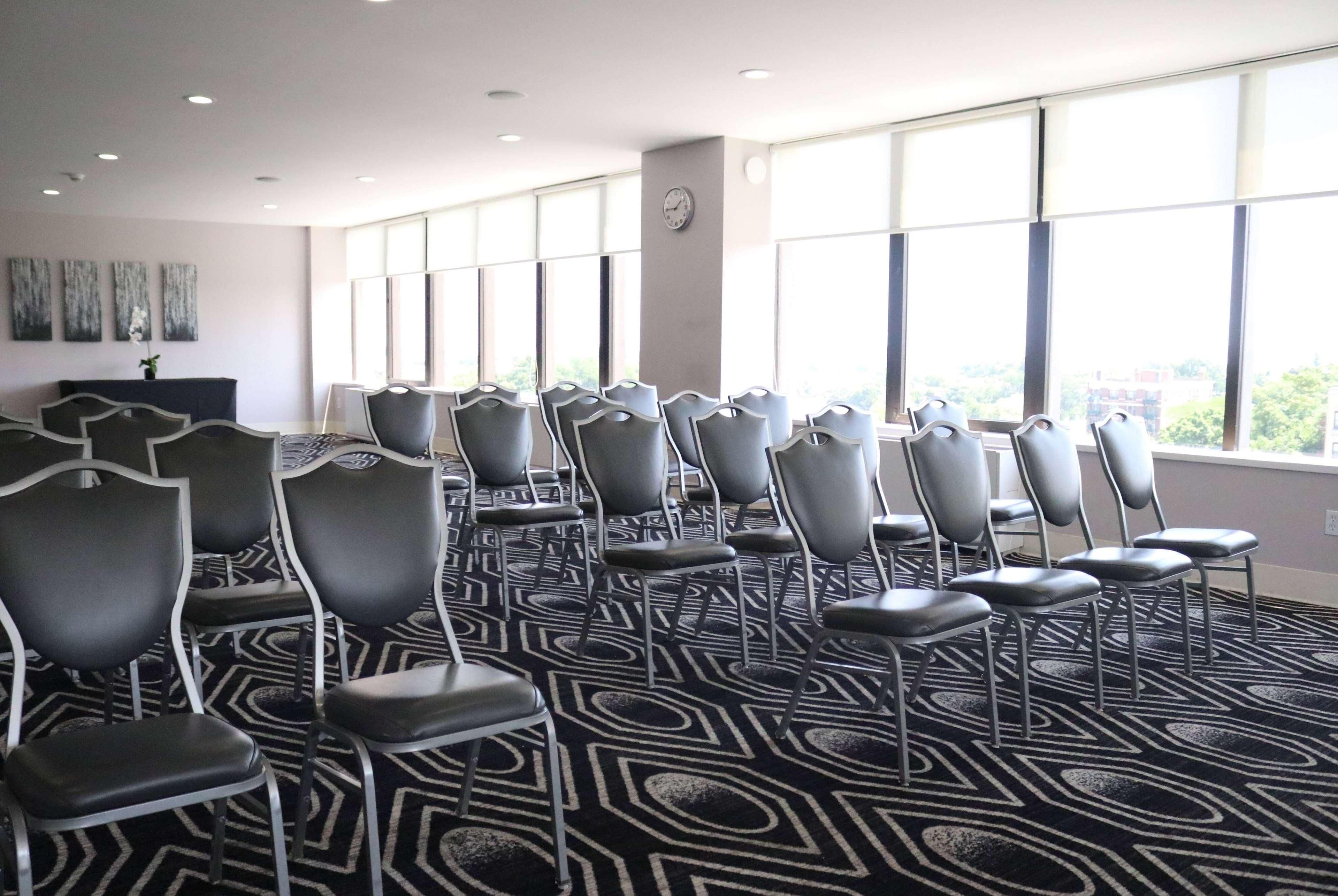 A conference room with rows of chairs, large windows, and a patterned carpet.