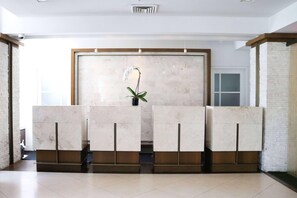 A reception area with marble counters, a potted plant, and a large window. - Hotel Noma Trademark Collection By Wyndham (New Rochelle)