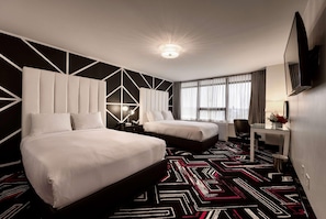 A hotel room with two beds, a desk, a chair, a TV, and a patterned carpet. - Hotel Noma Trademark Collection By Wyndham (New Rochelle)