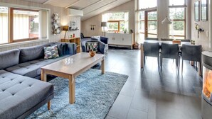 Een ruime woonkamer met een hoge plafond, een zithoek, een eettafel en een open haard.