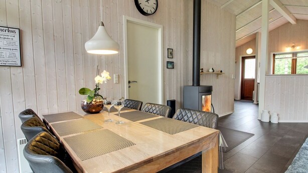 Een eethoek met een houten tafel, comfortabele stoelen, een hanglamp en een zichtbare klok aan de muur.