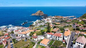 A coastal town with a prominent rocky island in the sea, residential buildings, and a marina. - Sea & Mountain by Atlantic Holiday (Porto Moniz)