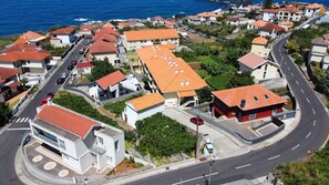 A coastal residential area with houses featuring red-tiled roofs, a curved road, and a clear view of the sea. - Sea & Mountain by Atlantic Holiday (Porto Moniz)