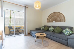 A modern living room with a grey sofa, a round coffee table, and a balcony with a table and chairs.