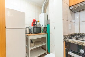 A compact kitchen with a microwave, kettle, and gas stove.