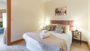 A neatly made bed with a blanket and towels, a headboard, two bedside lamps, a nightstand, and a wall art piece.