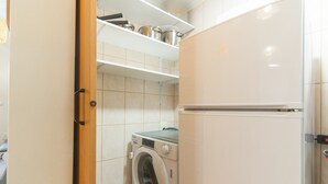 A compact kitchen with a washing machine, a refrigerator, and a shelf with pots.