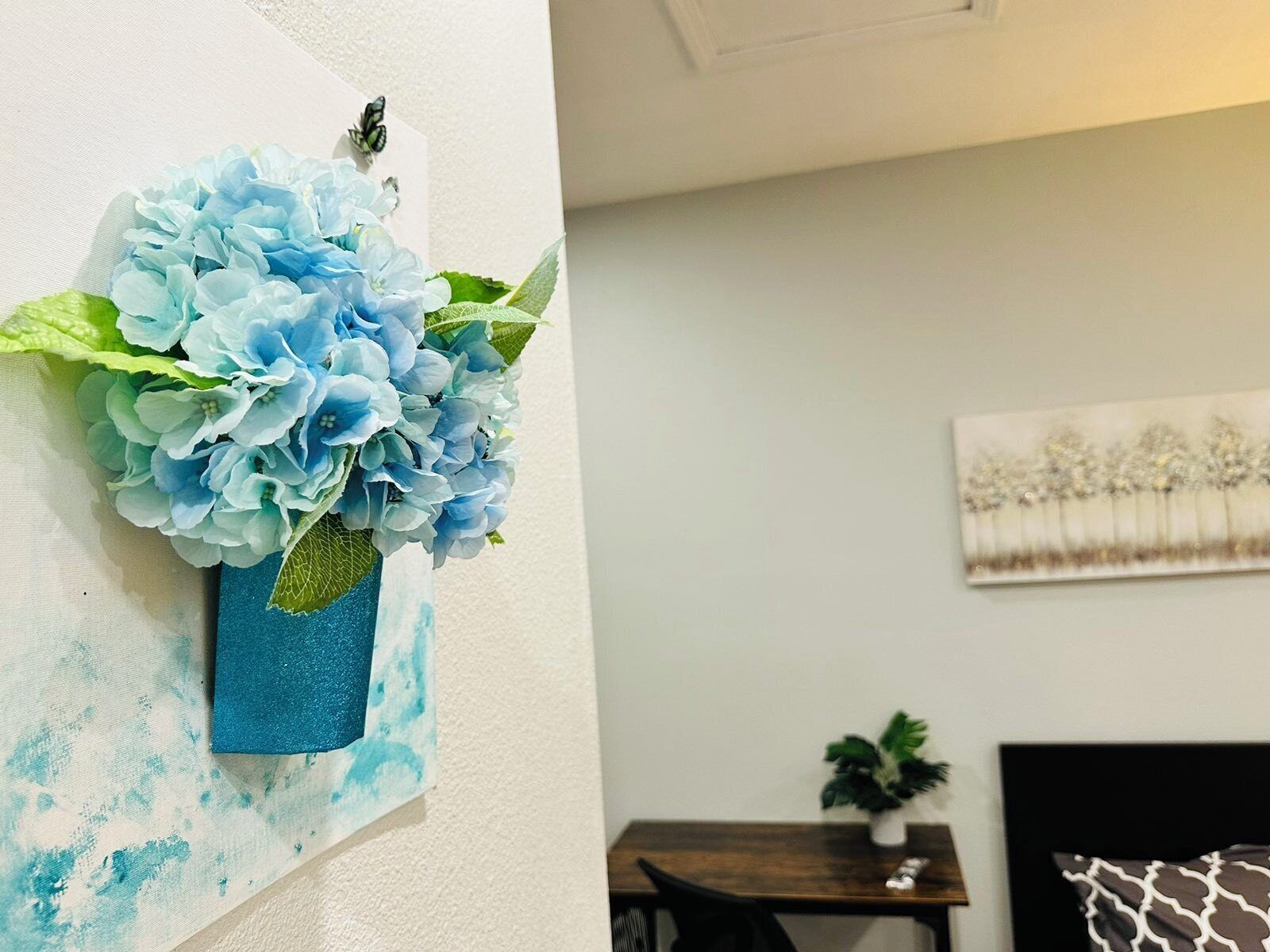 A room with a bed, a small table with a plant, and a wall-mounted artwork.