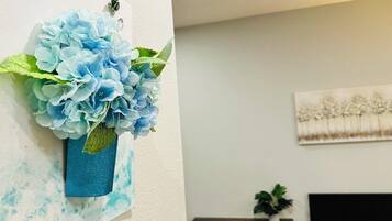 A room with a bed, a small table with a plant, and a wall-mounted artwork.