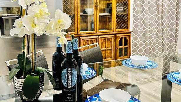 Een eethoek met een glazen tafel, blauwe en witte borden en een fles wijn.