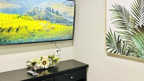 Een flatscreen televisie aan een muur bevestigd, een zwart bureau met een bloemenvaas, en een lijst met bladeren.