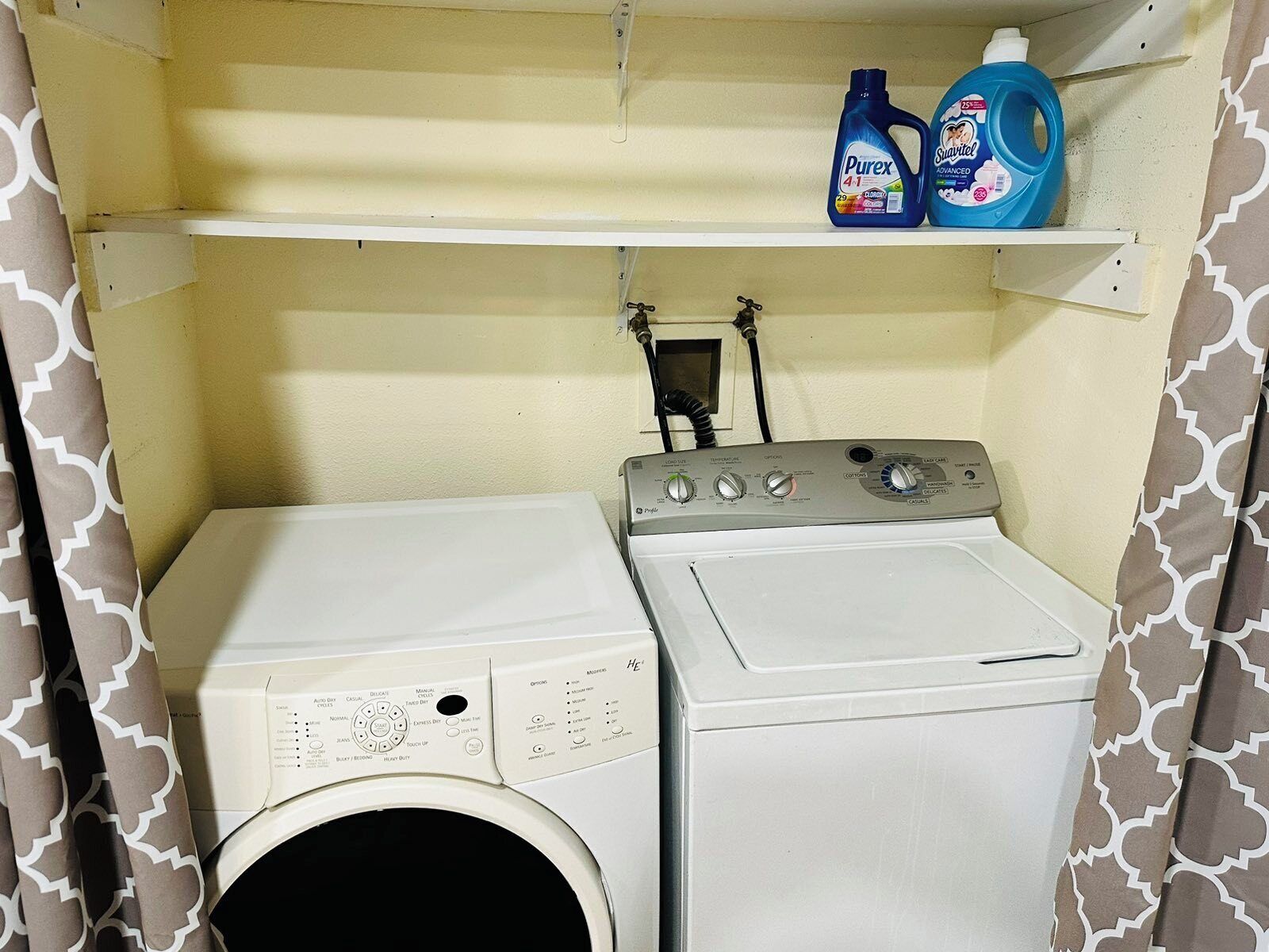 A compact laundry room with a front-loading washer and dryer, a shelf with detergent bottles, and a wall-mounted control panel.
