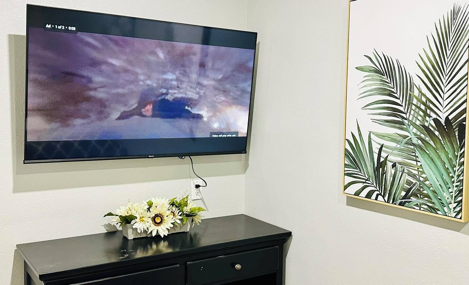 Ein flachbildfernseher an der Wand, ein schwarzer Konsolentisch mit einer Blumenvase und ein botanisches Bild in einem Rahmen.