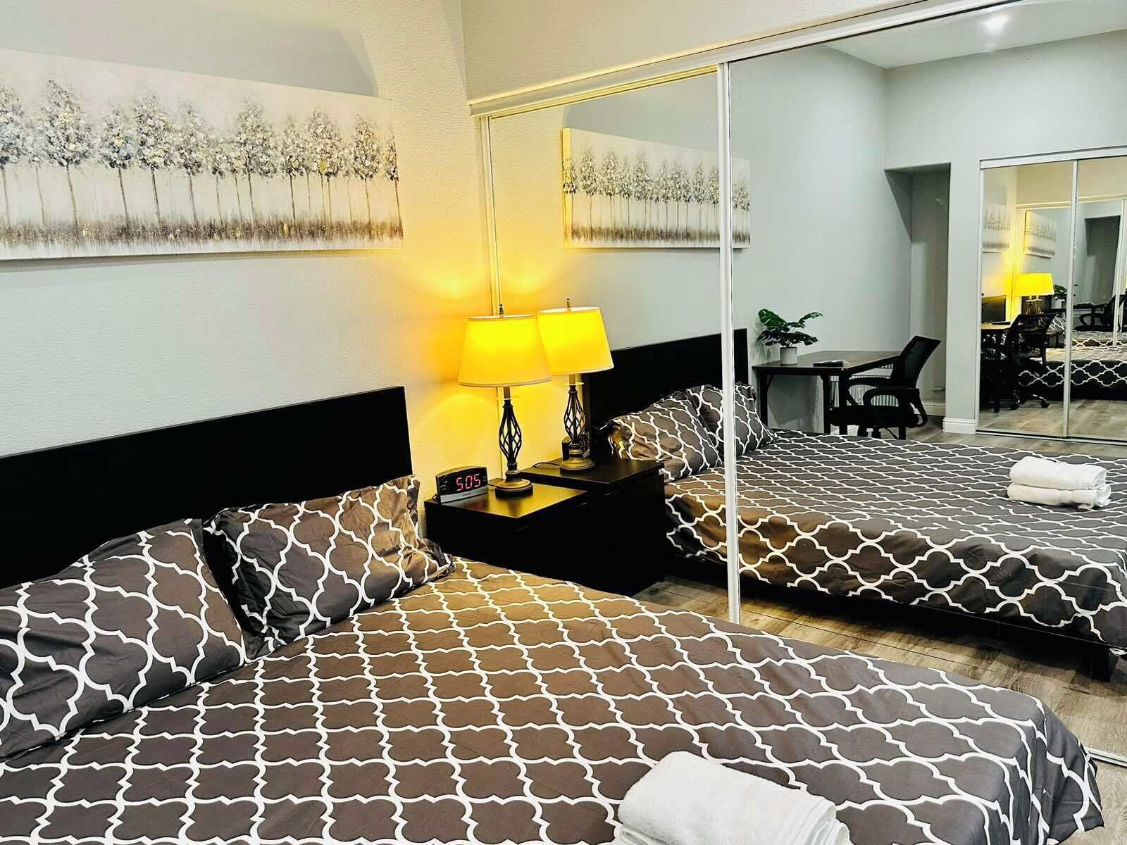 A hotel room with two beds, a large mirror, a desk, and a chair.
