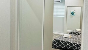 Een slaapkamer met een schuifdeur, een bed met beddengoed met een patroon, en een spiegel die de kamer weerspiegelt.
