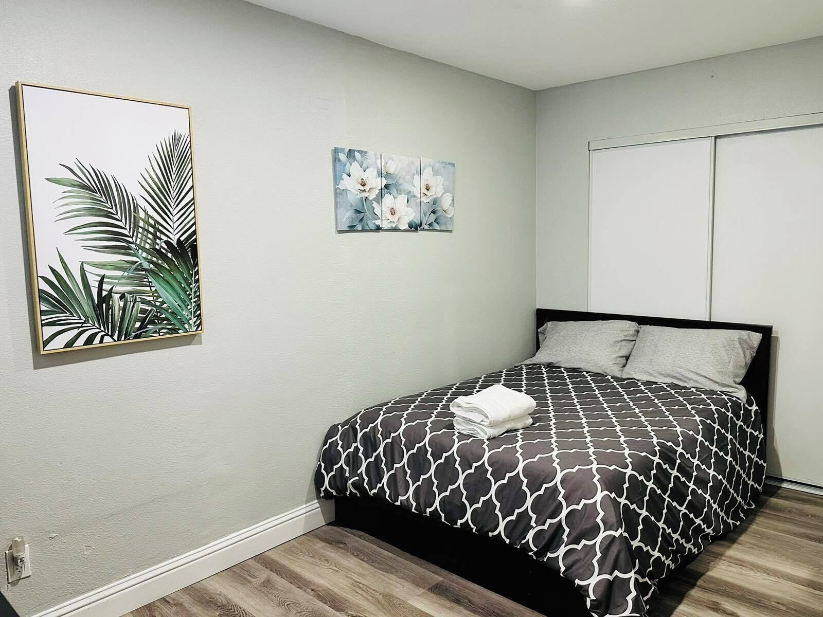 Une chambre à coucher avec un lit, une table de chevet, un tableau accroché au mur et une porte.