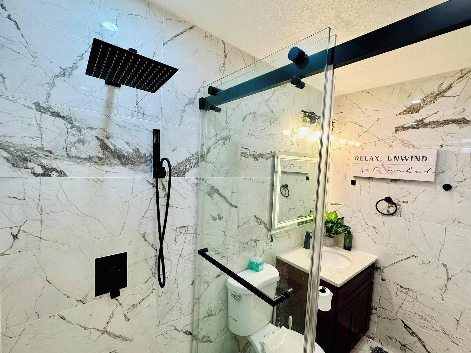Un baño moderno con cabina de ducha de vidrio, paredes de mármol, lavamanos e inodoro.