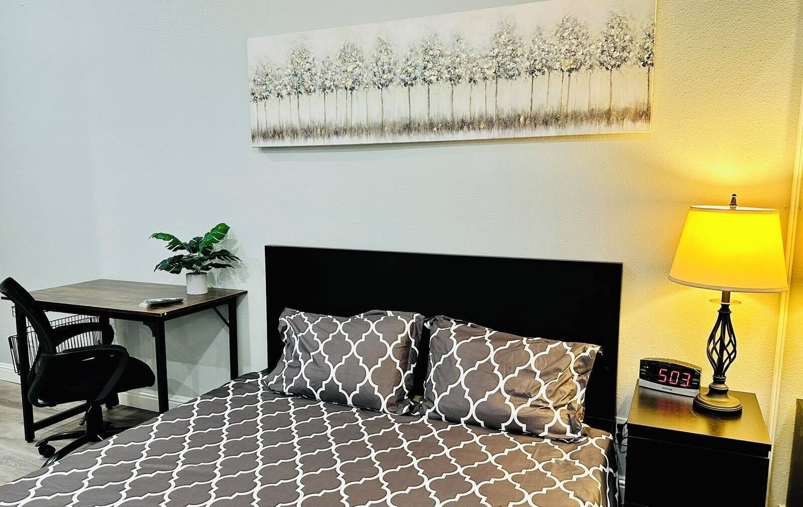 A hotel room with a bed, a desk, a chair, a lamp, and a painting on the wall.