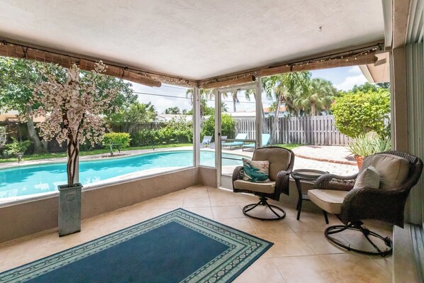 Relax by the pool with a view from this patio, featuring a comfortable seating area and lush greenery.