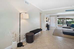 Relax in a spacious living area with a sofa, rug, and floor lamps, offering a connection to the outdoors through a large sliding glass door.