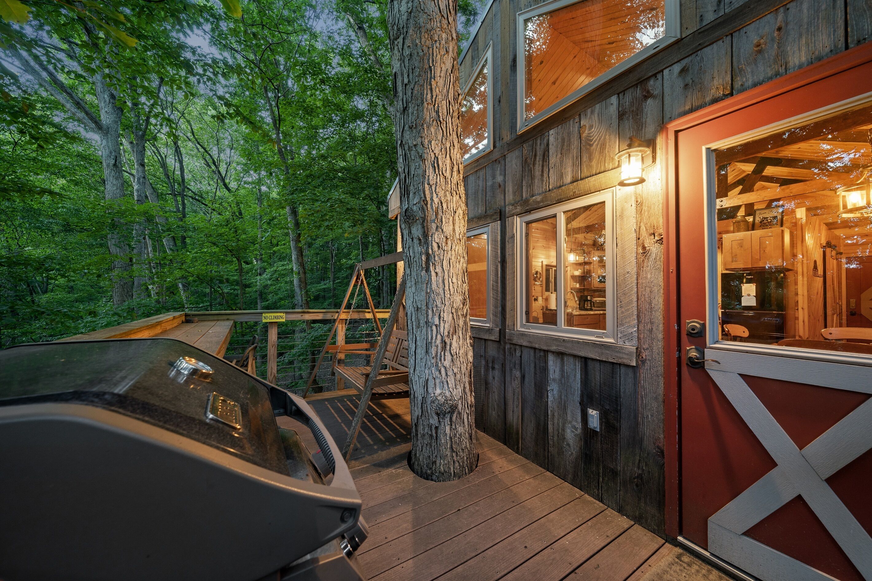 A wooden cabin with a deck, a car, and a red door.