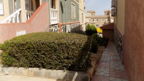 Une ruelle étroite bordée d’un beau massif de haies, avec un chemin pavé et un bâtiment doté d’un balcon et de fenêtres en arc de cercle.