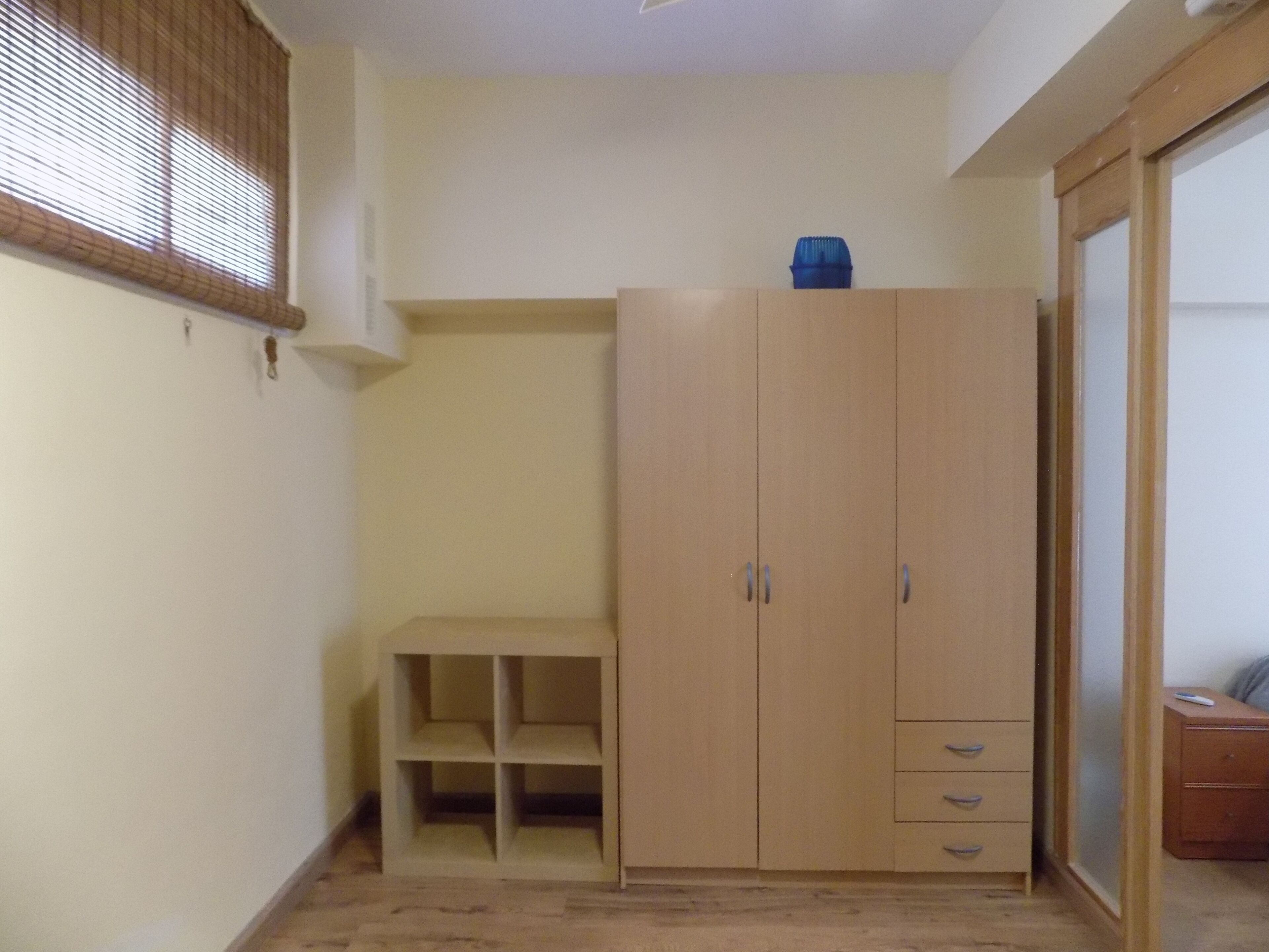 Een kamer met een houten garderobe, een klein bankje en een nachtkastje.