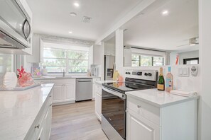 A modern kitchen with white cabinetry, stainless steel appliances, and a large window providing natural light.