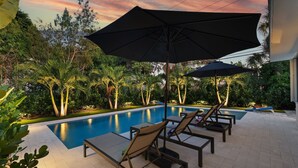 Un espace aménagé au bord de la piscine, avec des chaises longues et des parasols, entouré d’une végétation luxuriante.
