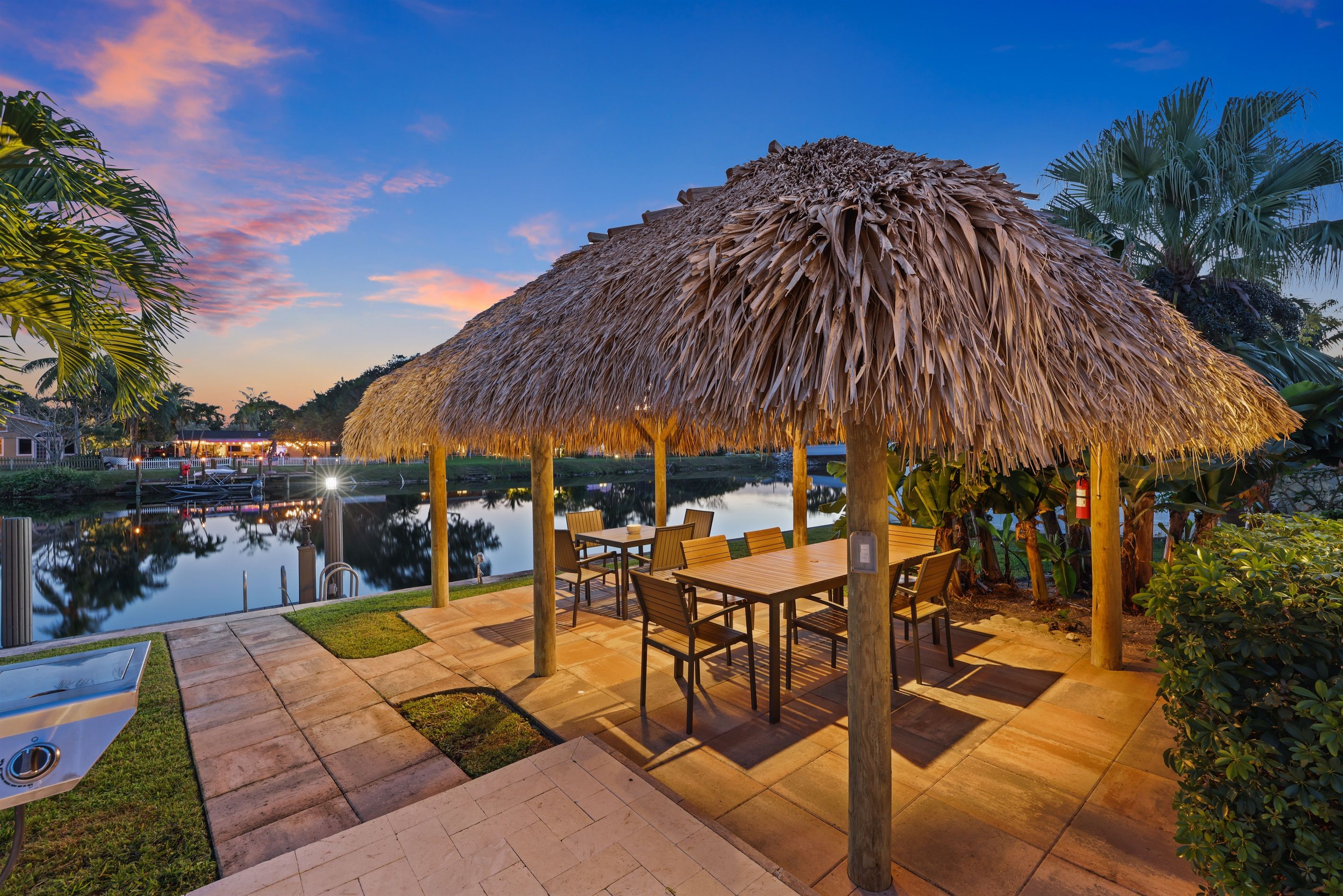 An outdoor patio with a thatched roof, a pool, and a dining area with tables and chairs.