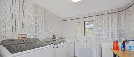 Wasruimte met een wasmachine, droger en een strijkhoek. Er is een raam met uitzicht op buiten.