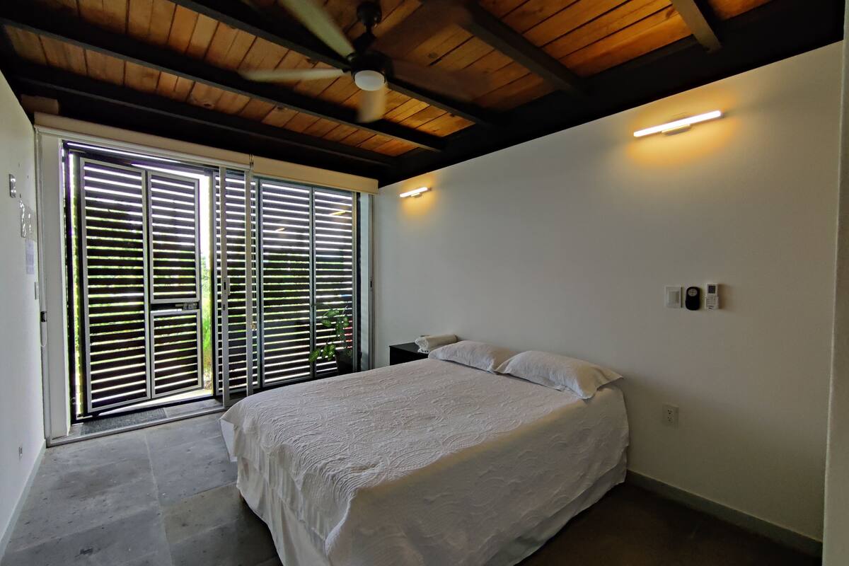Een slaapkamer met een bed, een plafondventilator, een schuifdeur met glas en een klein nachtkastje.