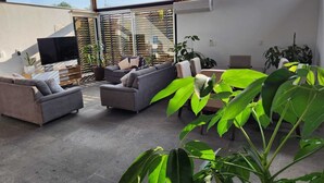 A modern living room with a large TV, comfortable seating, and a view through large windows.