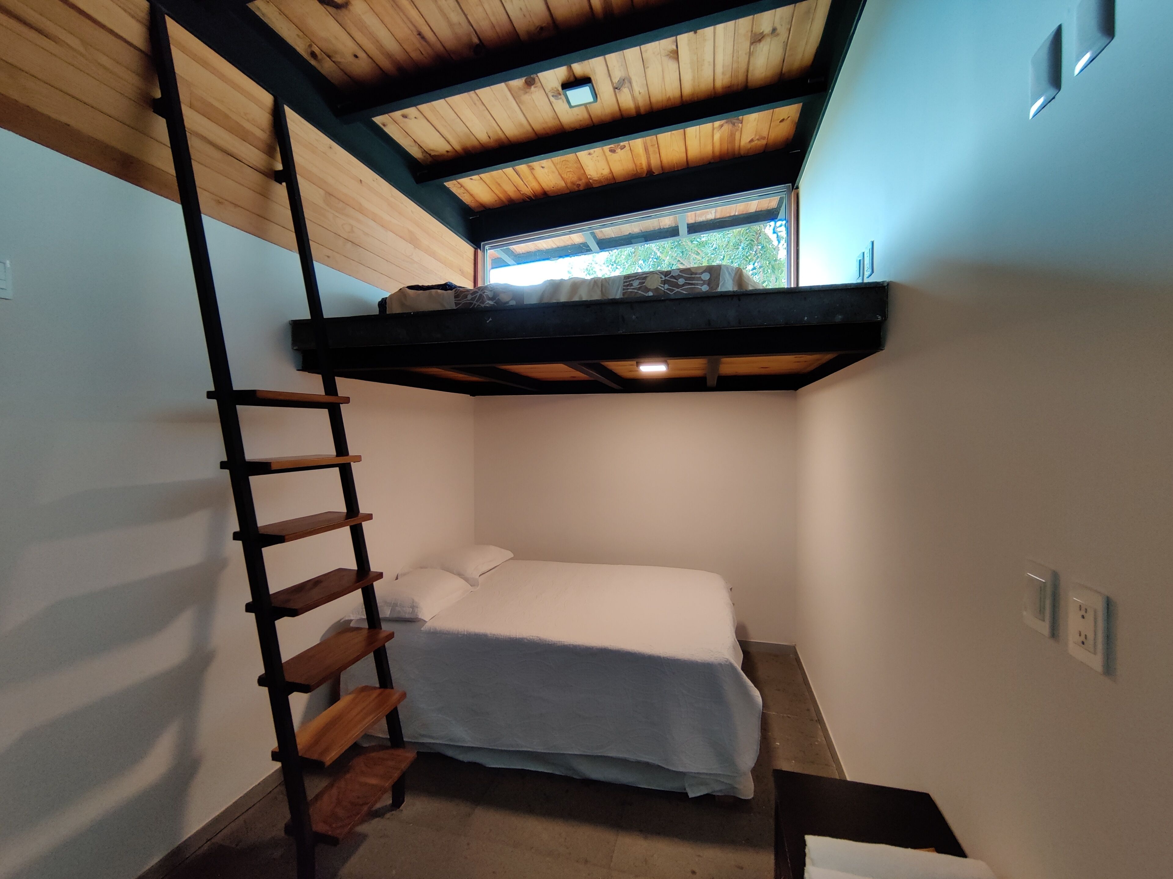Une petite pièce avec un lit superposé, une échelle en bois et une petite fenêtre.