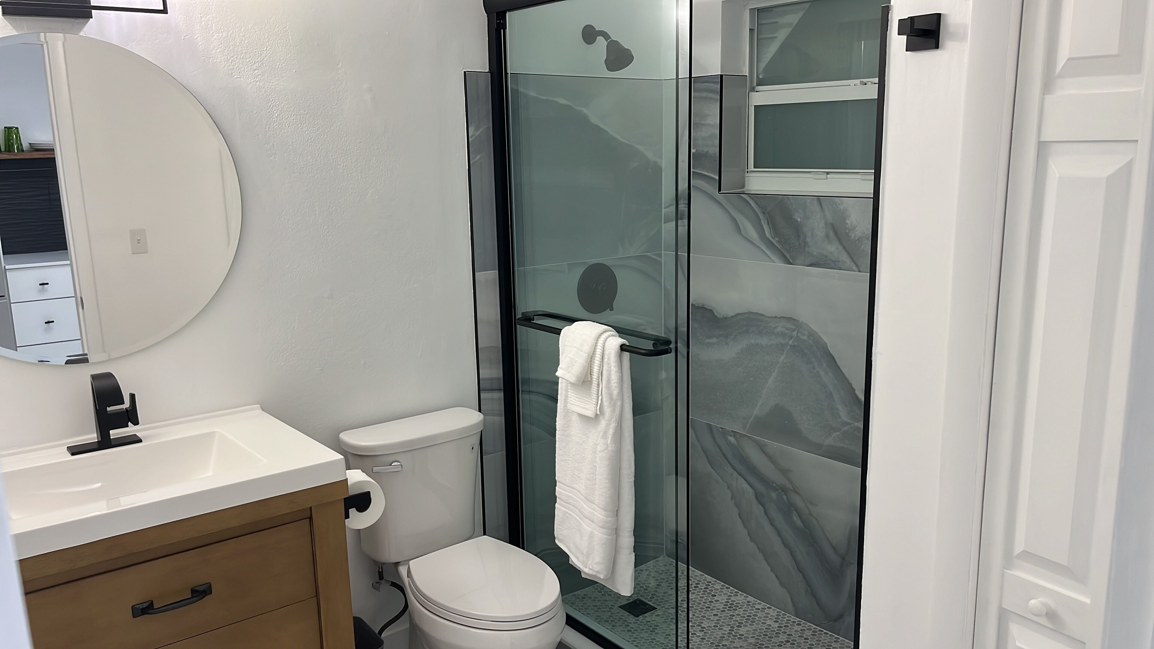 Een moderne badkamer met toilet, wastafel, spiegel en een douchecabine met glazen wanden.