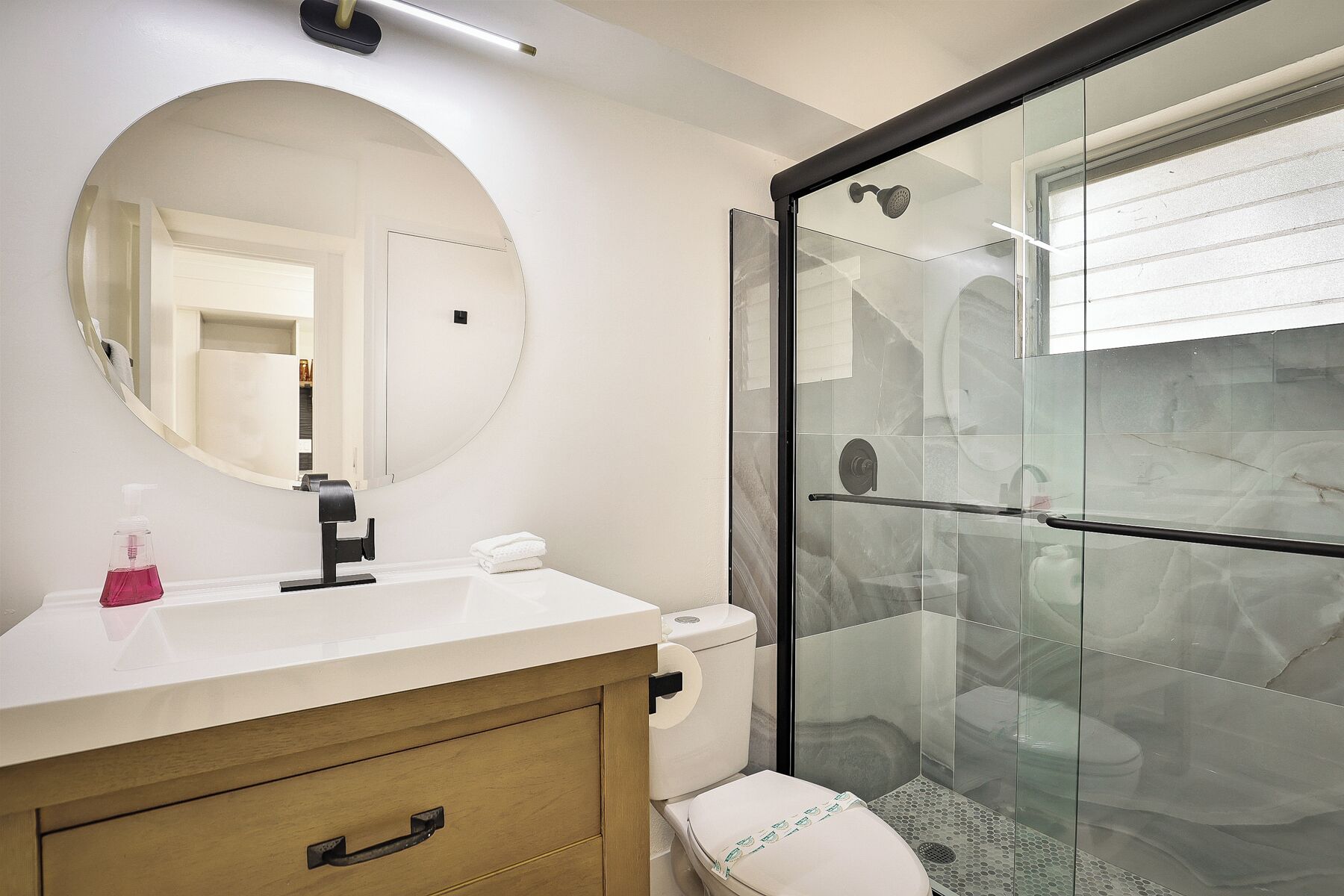 Un bagno con uno specchio rotondo, un lavandino bianco, un water e una cabina doccia in vetro.