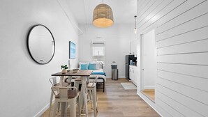 A modern, minimalist room with a wooden dining table and chairs, a bed with blue bedding, and a kitchen area with white cabinetry. - Stylish Downtown Loft, Walk to The Strand (Galveston)