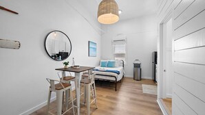 A compact room with a bed, a dining table with chairs, a round mirror, and a hanging light fixture. - Stylish Downtown Loft, Walk to The Strand (Galveston)